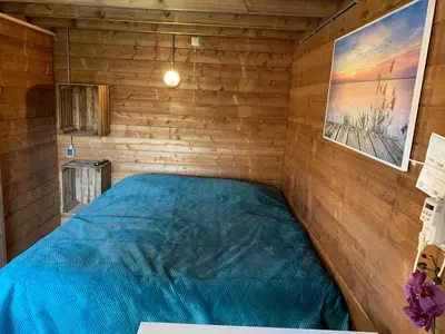 a bedroom with a blue bed in a wooden room at Chalet - B&B de Koog in Uitgeest