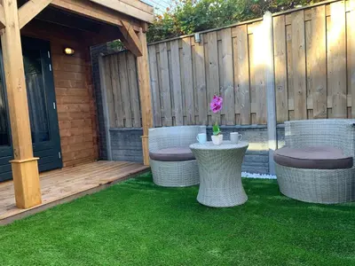 a patio with wicker chairs and a table on the grass at Chalet - B&B de Koog in Uitgeest