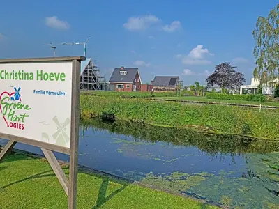 a sign in front of a river with a house at Christinahoeve Logies Oude Deel in Boskoop