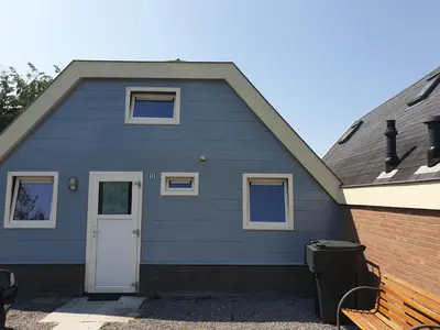 a blue house with a white door and a bench at Lovely Bungalow 8p close to beach and Amsterdam in Opmeer
