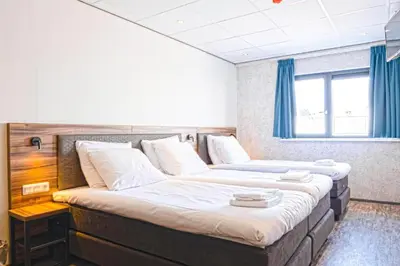 two beds in a room with blue curtains at Harbour Hotel IJmuiden in IJmuiden