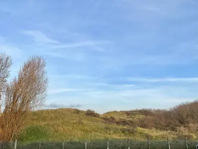 a fence in a field with a hill in the background at Alibi aan Zee in Wijk aan Zee