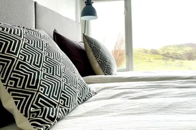 a bed with black and white pillows and a window at Alibi aan Zee in Wijk aan Zee
