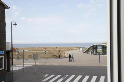 two people walking on a sidewalk near the ocean at Kusthuiskatwijk in Katwijk aan Zee