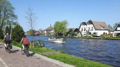 a couple of people riding bikes along a river with a boat at Woubrugge Logies in Woubrugge
