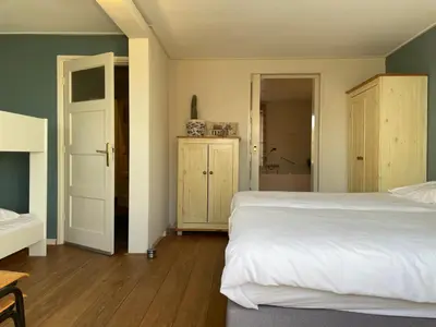 a bedroom with a white bed and a bathroom at Fijne vakantiehuizen 50 mtr van het strand in Egmond aan Zee