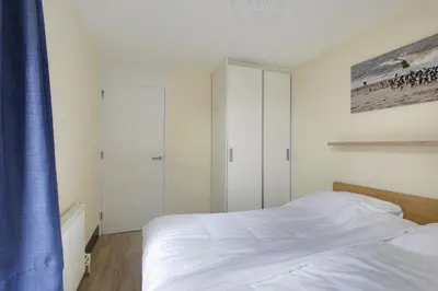 a bedroom with a white bed and a blue curtain at DE TRINTEL op 1e verdieping met ruim terras en zeezicht in Egmond aan Zee
