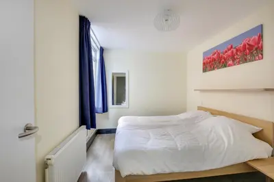 a bedroom with a white bed and a window at DE TRINTEL op 1e verdieping met ruim terras en zeezicht in Egmond aan Zee