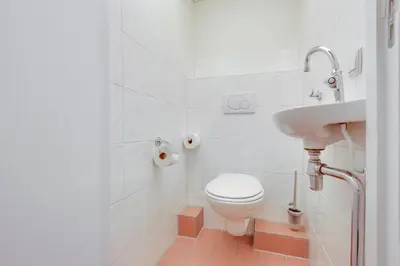 a white bathroom with a toilet and a sink at DE TRINTEL op 1e verdieping met ruim terras en zeezicht in Egmond aan Zee