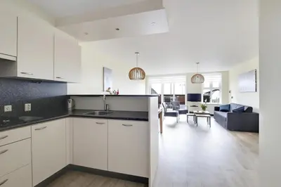 a kitchen with white cabinets and a living room at DE TRINTEL op 1e verdieping met ruim terras en zeezicht in Egmond aan Zee