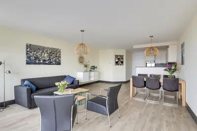a living room with a couch and a table and chairs at DE TRINTEL op 1e verdieping met ruim terras en zeezicht in Egmond aan Zee
