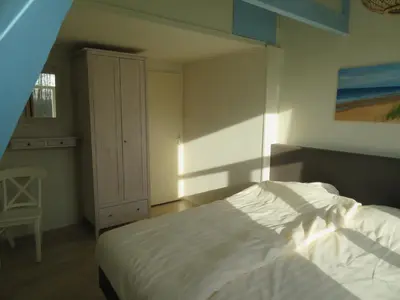 a bedroom with a white bed and a chair at Het Dijkstuk in Noordwijkerhout