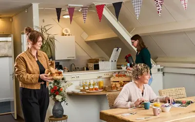two women standing in a kitchen with a woman sitting at a table at B&B Hartje Spakenburg in Spakenburg