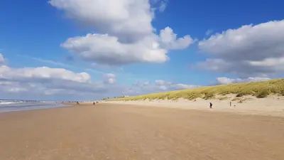 a beach with people walking on the sand and the ocean at 'Heerlijk Zomerhuis Vlakbij Strand en Duinen' in Egmond aan Zee
