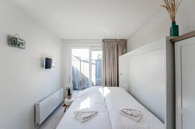 a white bedroom with a bed and a window at Studio Jadana in Zandvoort