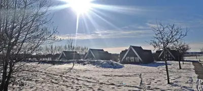 a group of houses in a snowy field with the sun at Hotelhuisje Warmenhuizen #F in Warmenhuizen