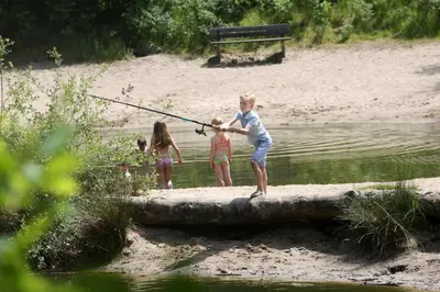 a group of children fishing on a log in the water at De Krakeling in Zeist