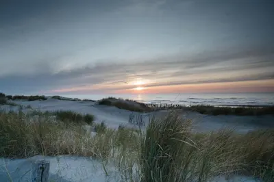 a sunset over a beach with sand and the ocean at Dune and Beach Villa with very large and beautiful Garden in Schoorl