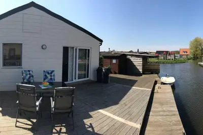a deck with a table and chairs next to a house at Ferienhaus Good Times mit eigenem Steg Ferienpark Vislust Ijsselmeer in Wervershoof
