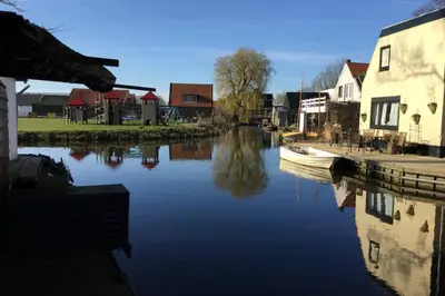 a river with a boat in the water next to houses at Ferienhaus Good Times mit eigenem Steg Ferienpark Vislust Ijsselmeer in Wervershoof