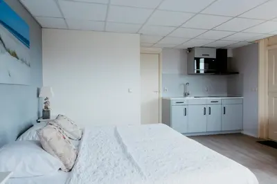 a bedroom with a white bed and a kitchen at Studio Parkweg in Bergen aan Zee
