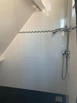 a shower in a bathroom with white tiles at B&BOosterweg3 Studio - Free private parking in Heemskerk