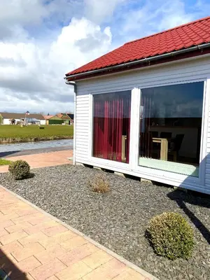 a building with a large window with a red roof at Ferienpark Vislust Modernes Holzhaus am Ijsselmeer mit eigenen Steg in Wervershoof