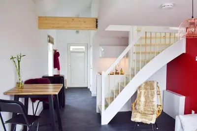 a living room with a staircase and a table and chairs at Mooi vakantiehuis prachtig gelegen aan het water in Rijpwetering
