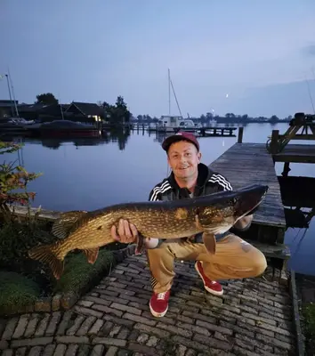 a man holding a fish in front of a dock at Mooi vakantiehuis prachtig gelegen aan het water in Rijpwetering
