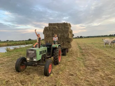 two children sitting on a tractor with a pile of hay at Boerencamping Swarthoeve in Wormer