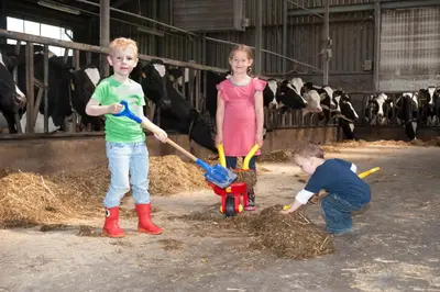 two children playing with a pile of hay in a barn with cows at Newhouse Logies in Zevenhoven