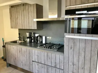 a kitchen with wooden cabinets and a stove top oven at Ferienhaus Genießen am Meer mit Wellnesszugang in Egmond aan Zee