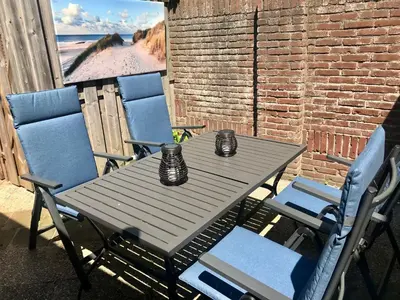 a table and chairs on a patio with a view of the beach at Ferienhaus Genießen am Meer mit Wellnesszugang in Egmond aan Zee