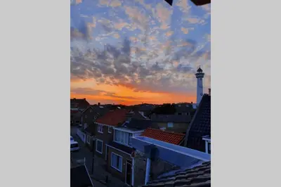 a view of a city with a lighthouse at sunset at Zomerhuis At Sea op top locatie in Egmond aan zee in Egmond aan Zee