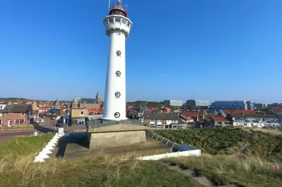 a lighthouse on a hill with a city in the background at Zomerhuis At Sea op top locatie in Egmond aan zee in Egmond aan Zee
