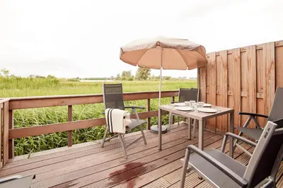 a wooden deck with a table and an umbrella at Dutchen Erfgoedpark De Hoop Appartementen in Uitgeest
