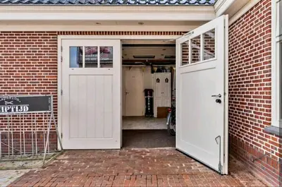 a garage with a white door and a brick wall at De Oude Smederij voor 2 personen in 't Veld in De Leijen