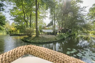 a boat in a river with trees and a house at 't Kleine eiland in Zuid-Scharwoude