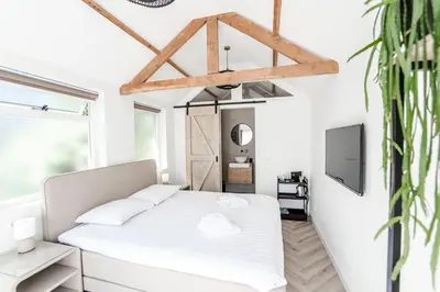 a white bedroom with a bed and a tv at Be So Suite in Zandvoort