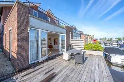 a house with a deck with a boat on the water at Meerzicht 20 - Waanzinnig uitzicht over het water! in Uitgeest