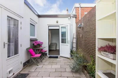 a small courtyard with a white door and pink chairs at Romana in Zandvoort