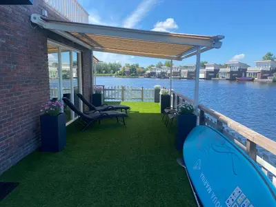 a patio with chairs and awning next to the water at Water Villa Minaro Vinkeveen in Vinkeveen