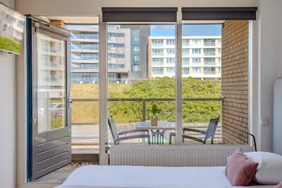 a bedroom with a bed and a balcony with a table and chairs at Perfect Stay Holiday, Moment at Sea in Egmond aan Zee