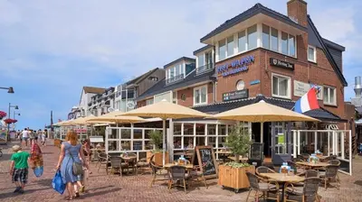 a group of people walking past a building with tables and chairs at Ferienhaus Abenteuer in Egmond aan Zee