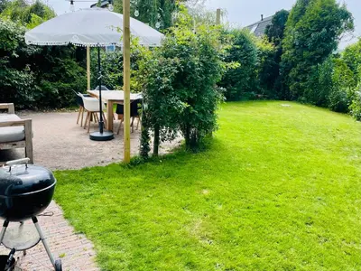 a grill and an umbrella in a yard at Have a nice stay! - Raaff-71 sfeervol huis direct bij bos, duin en strand in Noordwijk