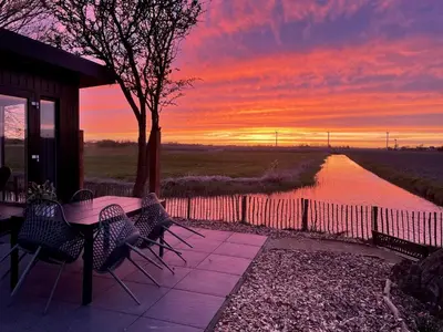a sunset on a patio with a table and chairs at Vogelvrij, vakantie woning met landelijk uitzicht en geheel omheinde tuin in Burgerbrug