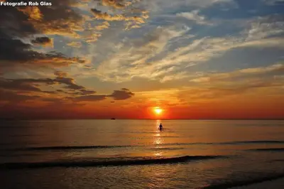a sunset on the beach with a person in the water at 4T4 Apartment B in Egmond aan den Hoef