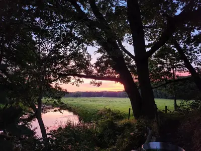 a sunset over a field and a river with trees at Huize Koempoelan in Naarden