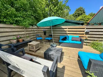a patio with a blue umbrella and furniture on a deck at Happy Little Maya Bee in Nieuwe-Niedorp