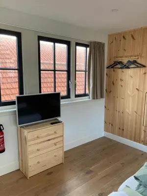 a bedroom with a flat screen tv and windows at Guesthouse Bonniehofje in Zandvoort